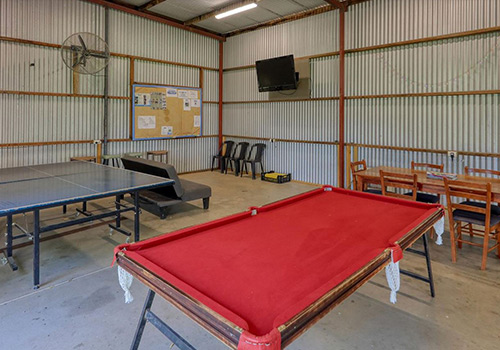 A recreational room at Barham Caravan Park featuring a red pool table, ping pong table, and seating areas with chairs and tables.