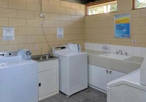 A communal laundry room at Barham Caravan Park, featuring white washing machines, dryers, and sinks with ample countertop space.