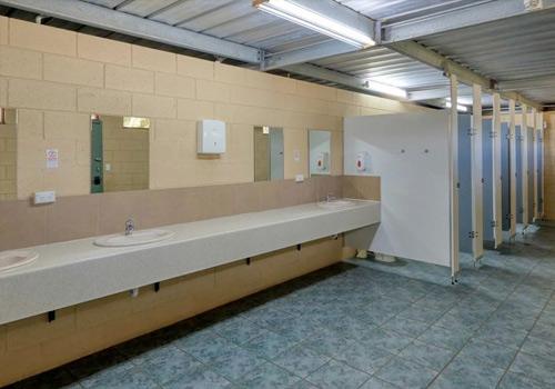 A clean and well-maintained public restroom with multiple sinks, mirrors, and stalls, featuring tiled floors and beige walls.